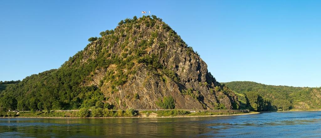 The Loreley, a steep rocky hill covered in trees, rising from the Rhine under a blue sky