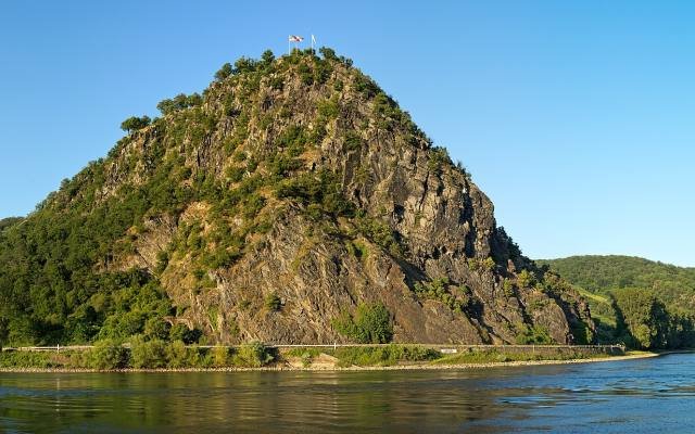 The Loreley, a steep rocky hill covered in trees, rising from the Rhine under a blue sky