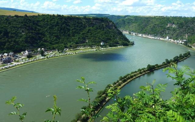The Rhine flowing north from the Loreley between wooded slopes, with the long harbour wall below