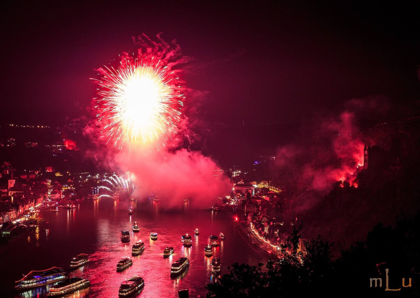 Red fireworks and flares lighting up the Rhine and a convoy of boats at night