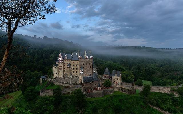 Eltz Castle rising from a forested valley in the morning mist