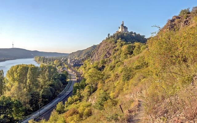 A narrow trail through dry grass on a steep slope above the Rhine, with the Marksburg on a hill beyond