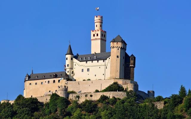 The white towers of the Marksburg on a wooded hilltop under a blue sky