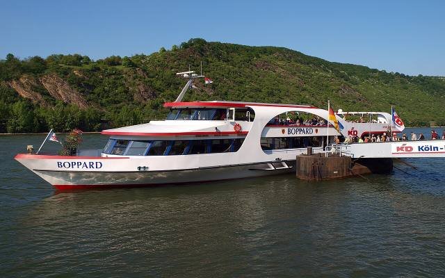 A white and red Rhine passenger boat moored on the river below wooded hills